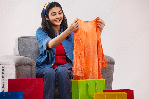 A young woman unpacking new dress sitting on sofa amidst colorful shoppingbags in her room. photo
