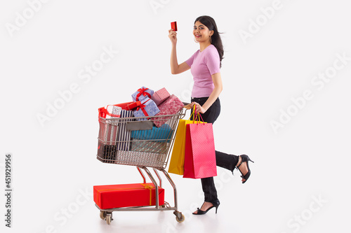 A young woman with credit card and colorful shoppingbags moving a cart full of gift boxes. photo