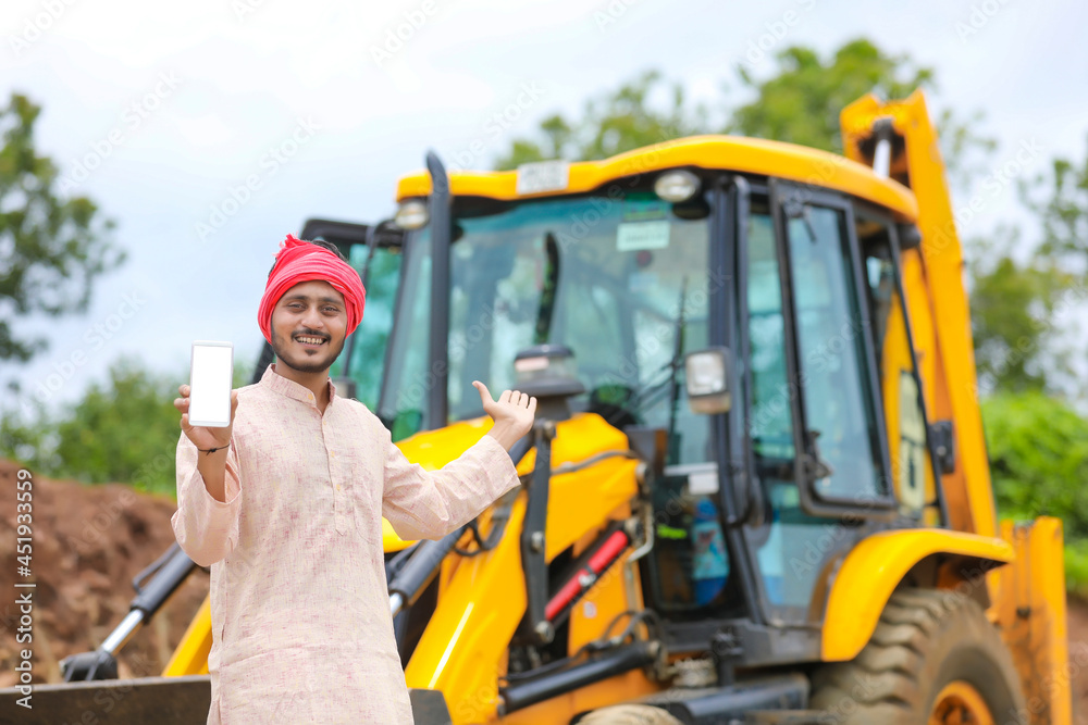 Indian farmer showing smartphone with his new earth mover machine equipment Indian farmer showing smartphone with his new earth mover machine equipment
