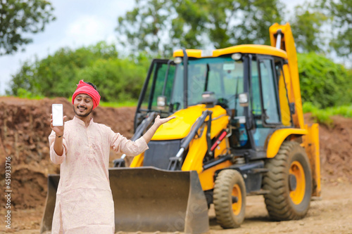 Indian farmer showing smartphone with his new earth mover machine equipment