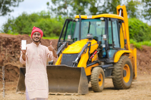 Indian farmer showing smartphone with his new earth mover machine equipment © Niks Ads