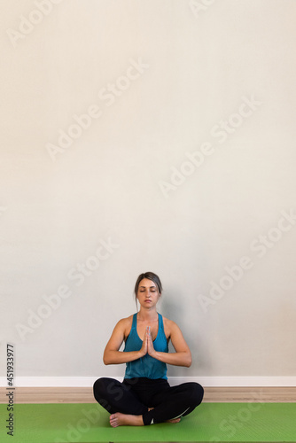 Young woman in blue t-shirt doing yoga at her home. Girl doing yoga at home on a green rug. Place for your text. Vertical frame