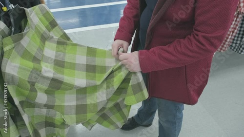Pregnant woman chooses a roomy, green, flannelette plaid shirt in the store to buy. The concept of buying new clothes, fashion, beauty and an active lifestyle while carrying a child. Hands close up photo