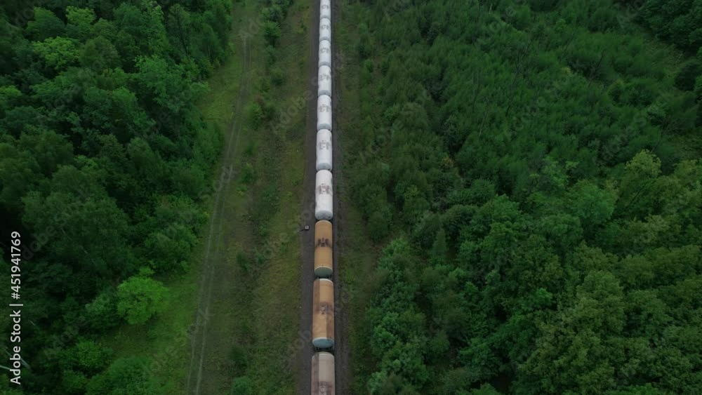 The train transports tanks of crude oil among virgin ecological green forests. Aerial view.