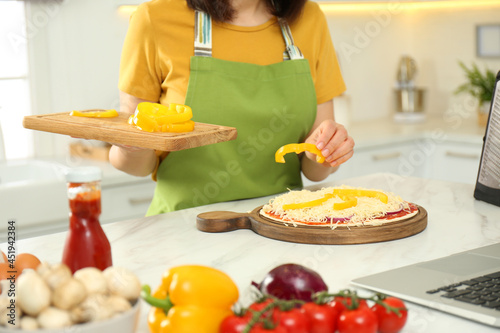 Woman making pizza while watching online cooking course via laptop in kitchen  closeup