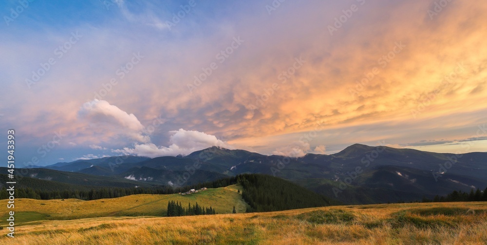 Traditional alpine house  and mountain pastures at sunset in summer. Panoramic view on Mountain valley, summits,  meadows and colorful sky at sunset in Alp. Mountain landscape with purple sky at dusk.