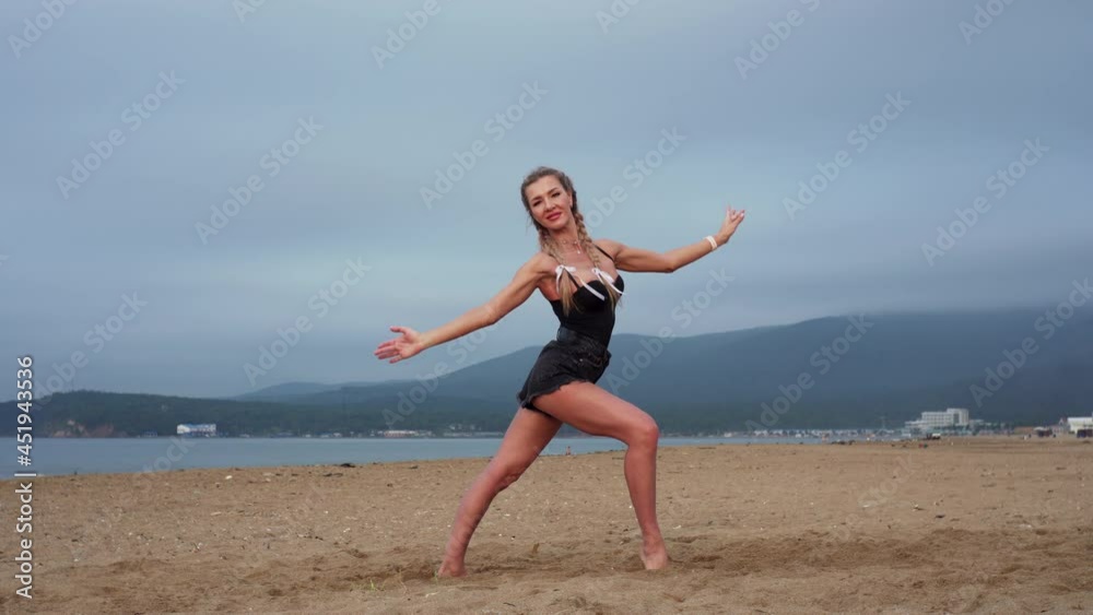 Pretty young woman with plaits is looking into the camera and moving in a sexy way on the beach. Misty mountains are on the background. Morning Pretty young woman with plaits is looking into the camera and moving in a sexy way on the beach. Misty mountains are on the background. Morning