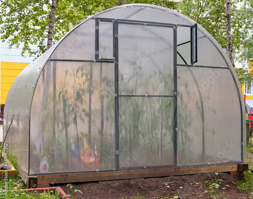 Handmade greenhouse from a metal framework and a polyethylene film on a farmer's land plot. Greenhouse Hotbed for vegetable seedlings.
