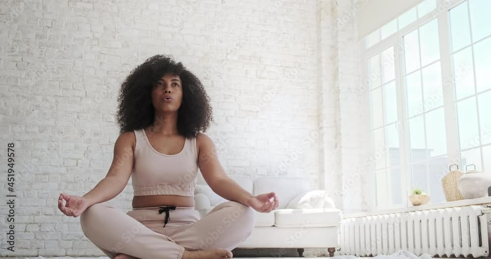 Yoga and breathing techniques practiced by a young, cheerful mixed-race woman. At home, a black woman practices calm relax harmony Zen mindfulness meditation. Self-isolation of Coronavirus Covid 19.