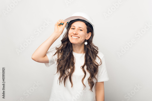 Happy young woman is smiling at the camera and wearing a white hard hat.