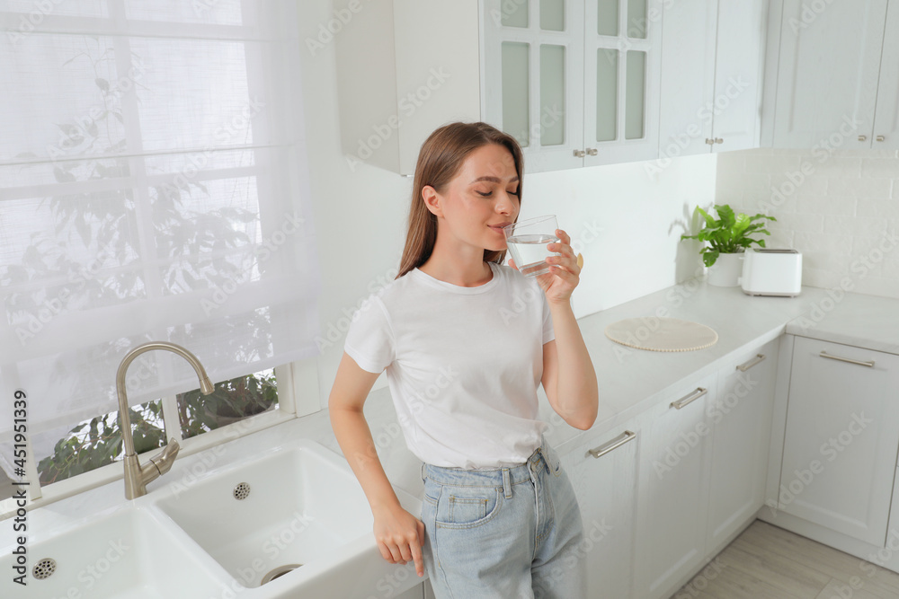 Woman drinking tap water from glass in kitchen Woman drinking tap water from glass in kitchen
