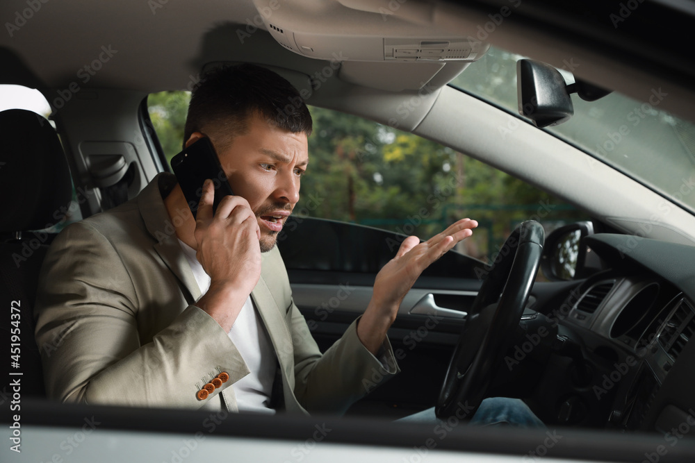 Stressed businessman talking on phone in driver's seat of modern car