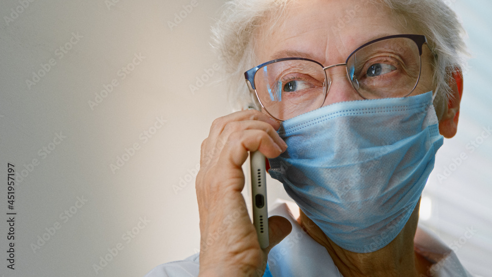 Mature woman doctor in protective mask and glasses talks on cell phone Mature woman doctor in protective mask and glasses talks on cell phone