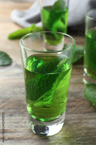 Delicious mint liqueur with green leaves on wooden table, closeup