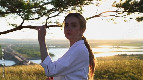 Swords training - young pretty woman in white shirt waving with a sword on nature at early evening on nature - looking in the camera photo