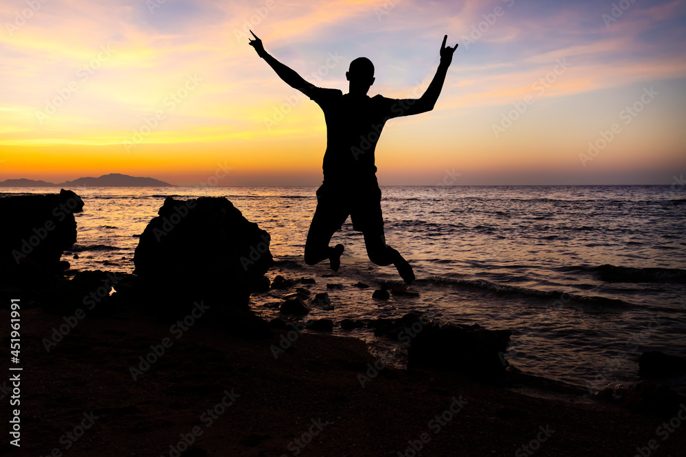 Man jumping on tropical beach with sunset sky and island background.