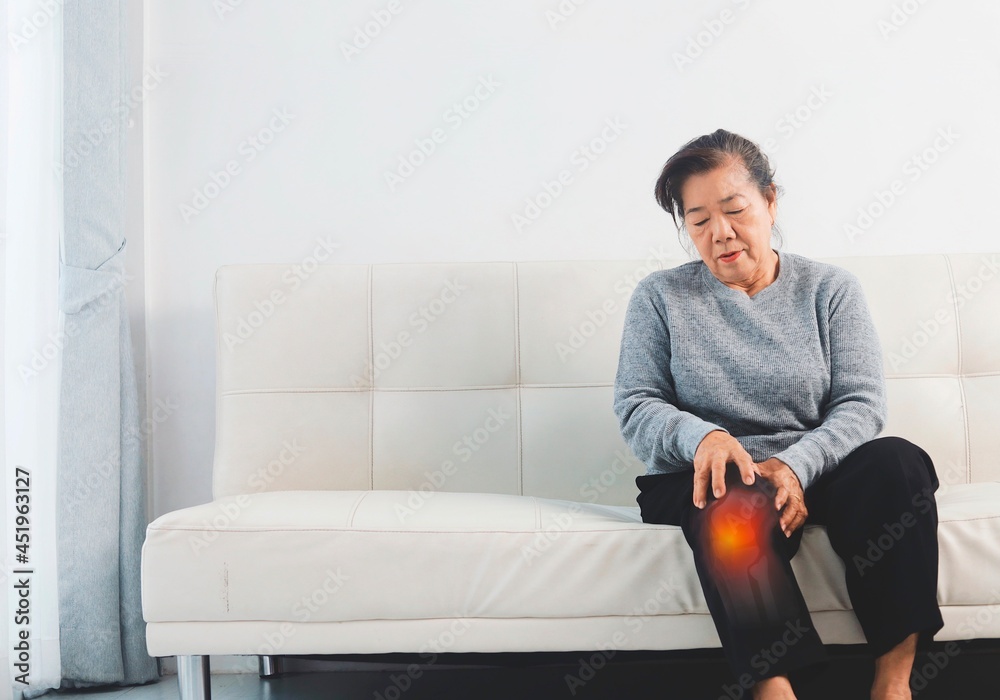 Elderly woman  suffering from knee pain sitting on sofa 