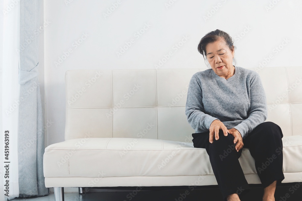 Senior woman suffering from knee pain sitting on sofa Senior woman suffering from knee pain sitting on sofa