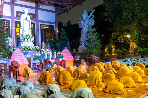Monks and Buddhists are reverently bowing to Buddha during evening ceremony for Amitabha Buddha at an ancient temple in Ho Chi Minh City, Vietnam