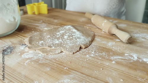 Child's hands rolling out dough for christmas cookies. pouring white wheat flour onto dough. Mom's assistant, Preparing for the winter holidays.