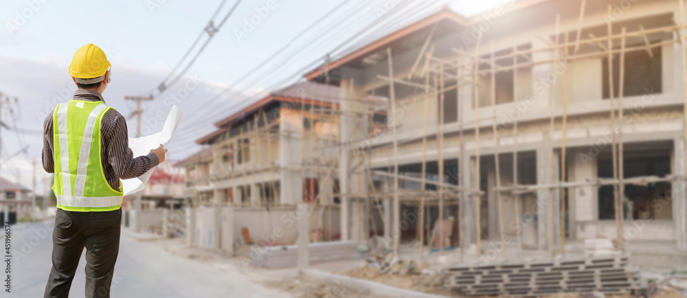 young professional engineer in protective helmet and blueprints paper at the house building construction site young professional engineer in protective helmet and blueprints paper at the house building construction site