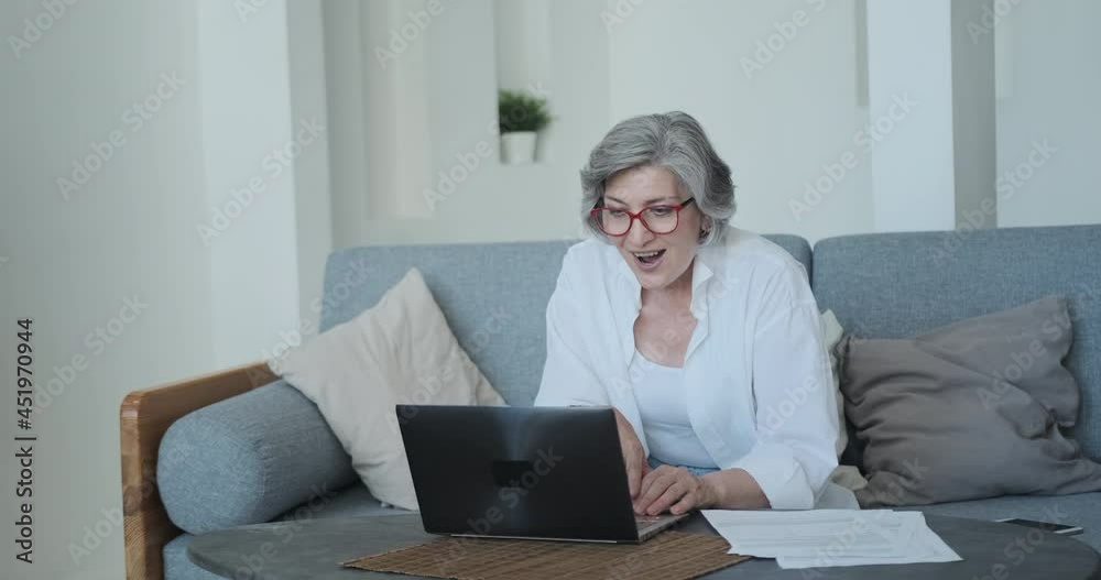 An excited senior woman is actively rejoicing and expressing her emotions about winning the online lottery. Big earnings from investing in cryptocurrency and bitcoins. Success comes in old age.