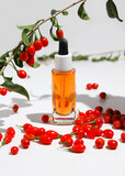 Goji berry seed oil in glass dropper bottle and fresh goji berries on table.