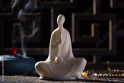 A small white Buddha figure sits with burner censer on black background