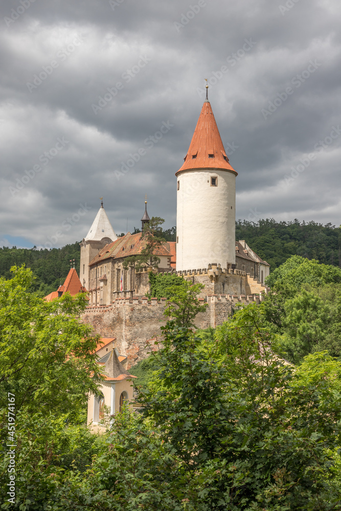 sunlit medieval castle with a round tower on a background of steel-gray clouds