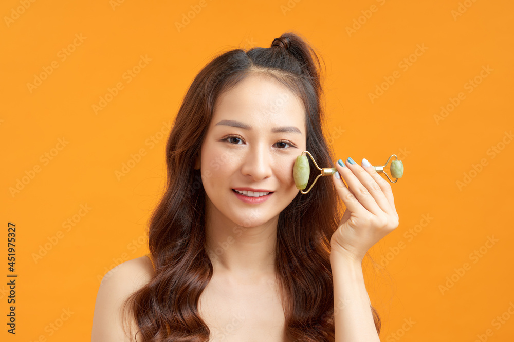 beautiful naked asian girl massaging face with jade roller isolated on yellow orange beautiful naked asian girl massaging face with jade roller isolated on yellow orange