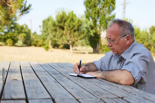 old man writing his diary in the park on a sunny day