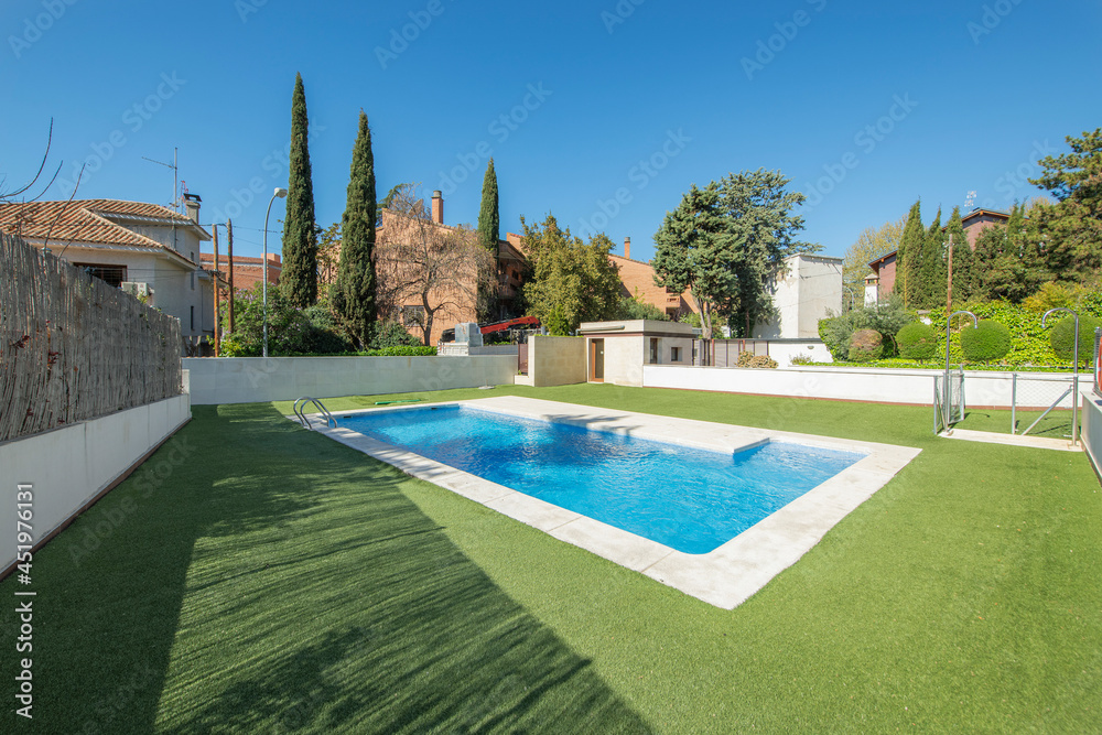 Summer pool surrounded by green grass with white marble go on a sunny day