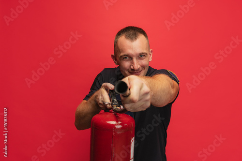 Fire safety. Portrait of young smiling man with extinguisher posing over red background. photo