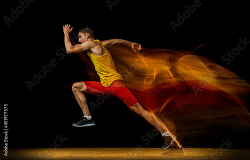 Portrait of young man, professional male athlete, runner in motion and action isolated on dark background. Stroboscope effect.