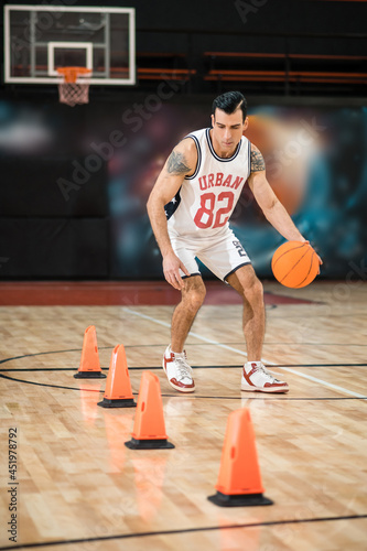 Tattoed man in white shportswear playing basket-ball