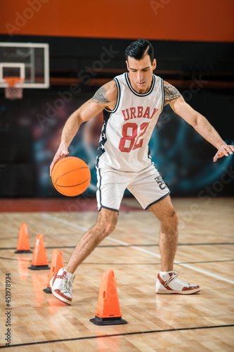 Tattoed man in white shportswear playing basket-ball and looking involved