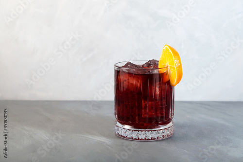 Glass of Boulevardier cocktail with big ice cubes and orange slice. Classic alcoholic drink composed of whiskey, sweet vermouth, and Campari photo