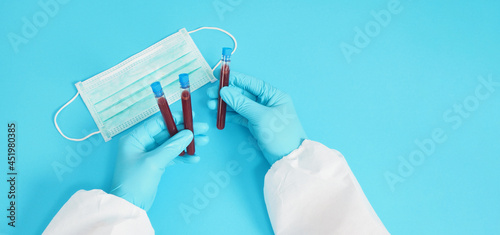 Hand with PPE suite and Hand is holding Blood test tubes and wearing medical glove ,face mask on blue background.