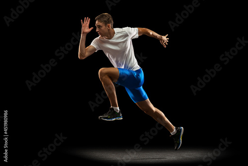 One muscular, sportive man, male athlete, runner training isolated on dark studio background with spotlight. Concept of action, motion, youth, healthy lifestyle.