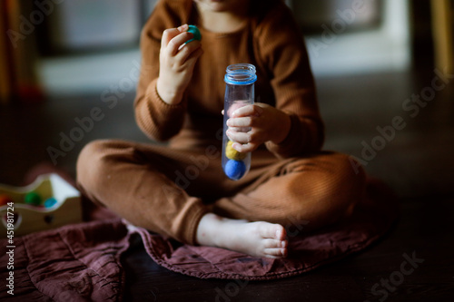 Cute european child on the floor playing with balls and probe, the child studies the colors using the Ira. Sensory Development and Domestic Lessons, Dark Style in the Real Interior