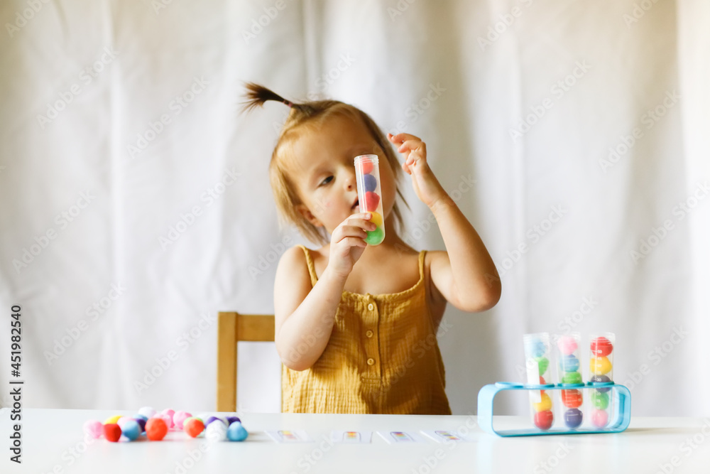 Cute Caucasian child on the table plays with balls and test tubes, the child studies the color using the game. Sensory development and home lessons Cute Caucasian child on the table plays with balls and test tubes, the child studies the color using the game. Sensory development and home lessons
