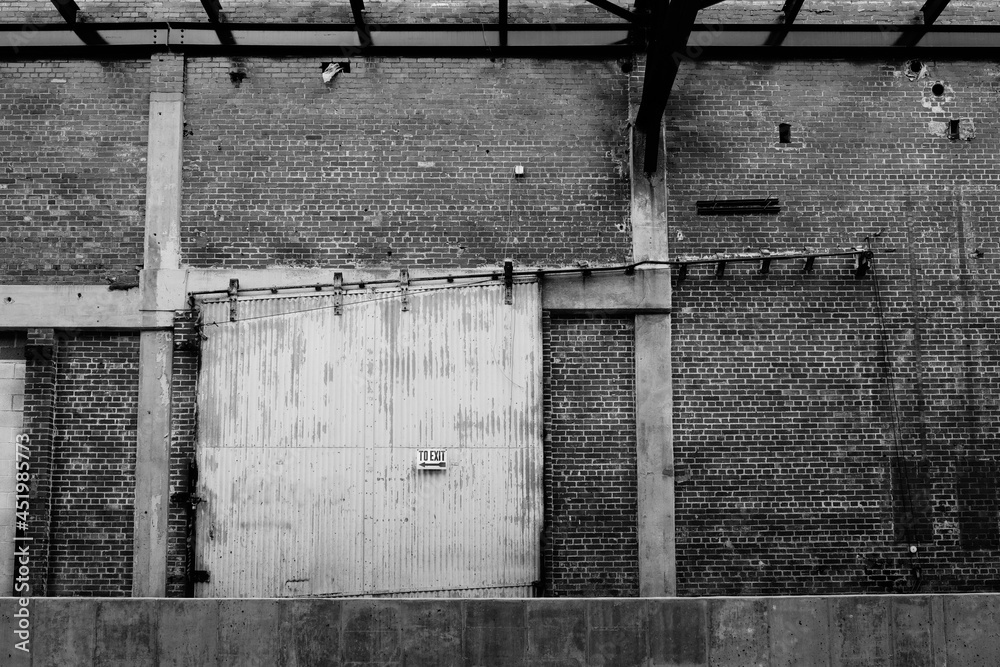 Rusting, sliding old warehouse door with angled track and exit sign