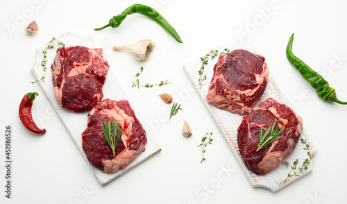 raw piece of beef ribeye with rosemary, thyme on a white table, top view