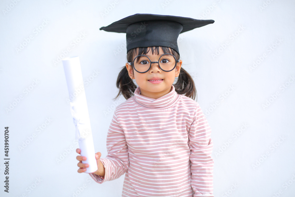 A little girl asia looks happy while celebrating his graduation and holding a diploma and graduation cap which increases the development and enhances outside the classroom learning skills concept. A little girl asia looks happy while celebrating his graduation and holding a diploma and graduation cap which increases the development and enhances outside the classroom learning skills concept.