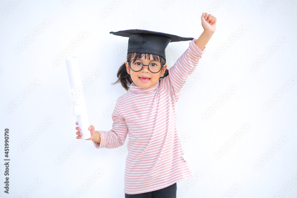 A little girl asia looks happy while celebrating his graduation and holding a diploma and graduation cap which increases the development and enhances outside the classroom learning skills concept. A little girl asia looks happy while celebrating his graduation and holding a diploma and graduation cap which increases the development and enhances outside the classroom learning skills concept.