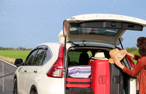 Closeup of woman's hand preparing luggage, suitcases and other things at rear side of white car. Preparing for lovely family holiday. 