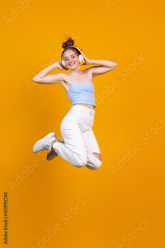 Vertical image of young cute girl jumping isolated on yellow studio background. Female fashion model in casual clothes. Concept of human emotions, natural beauty, youth