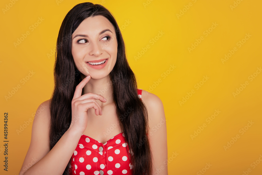 Portrait of minded curious woman look empty space finger chin wear dotted dress on yellow background Portrait of minded curious woman look empty space finger chin wear dotted dress on yellow background
