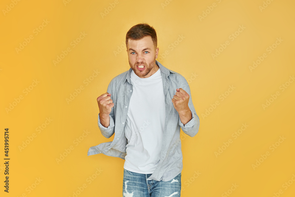 Fells anger. Young man in casual clothes standing indoors in the studio Fells anger. Young man in casual clothes standing indoors in the studio