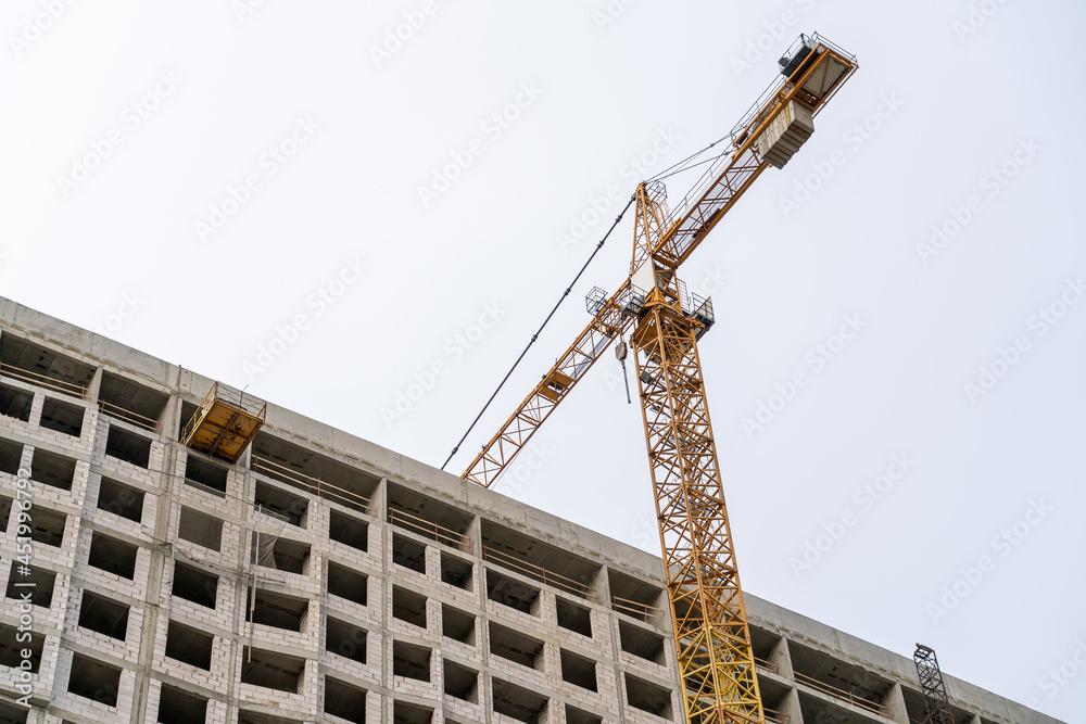Yellow construction tower crane and unfinished residential building against grey sky